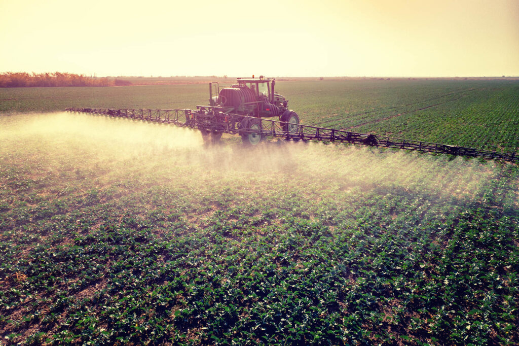 Tractor spraying fertilizer or pesticides on field with sprayer